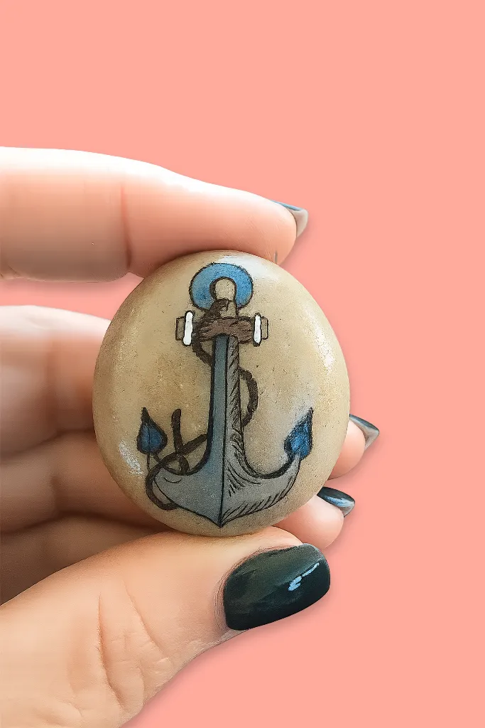 anchor painted pebble held between forefinger and thumb of left hand
