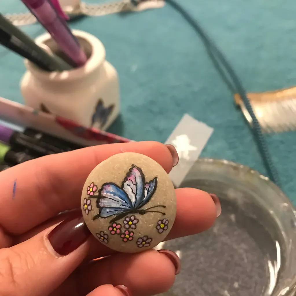butterfly and flowers painted on a light pebble held in the hand of a lady