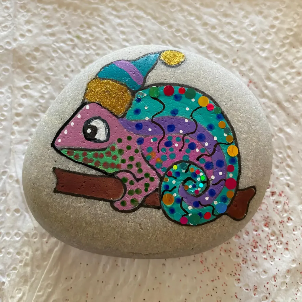light stone painted with colourful chameleon wearing pom-pom hat