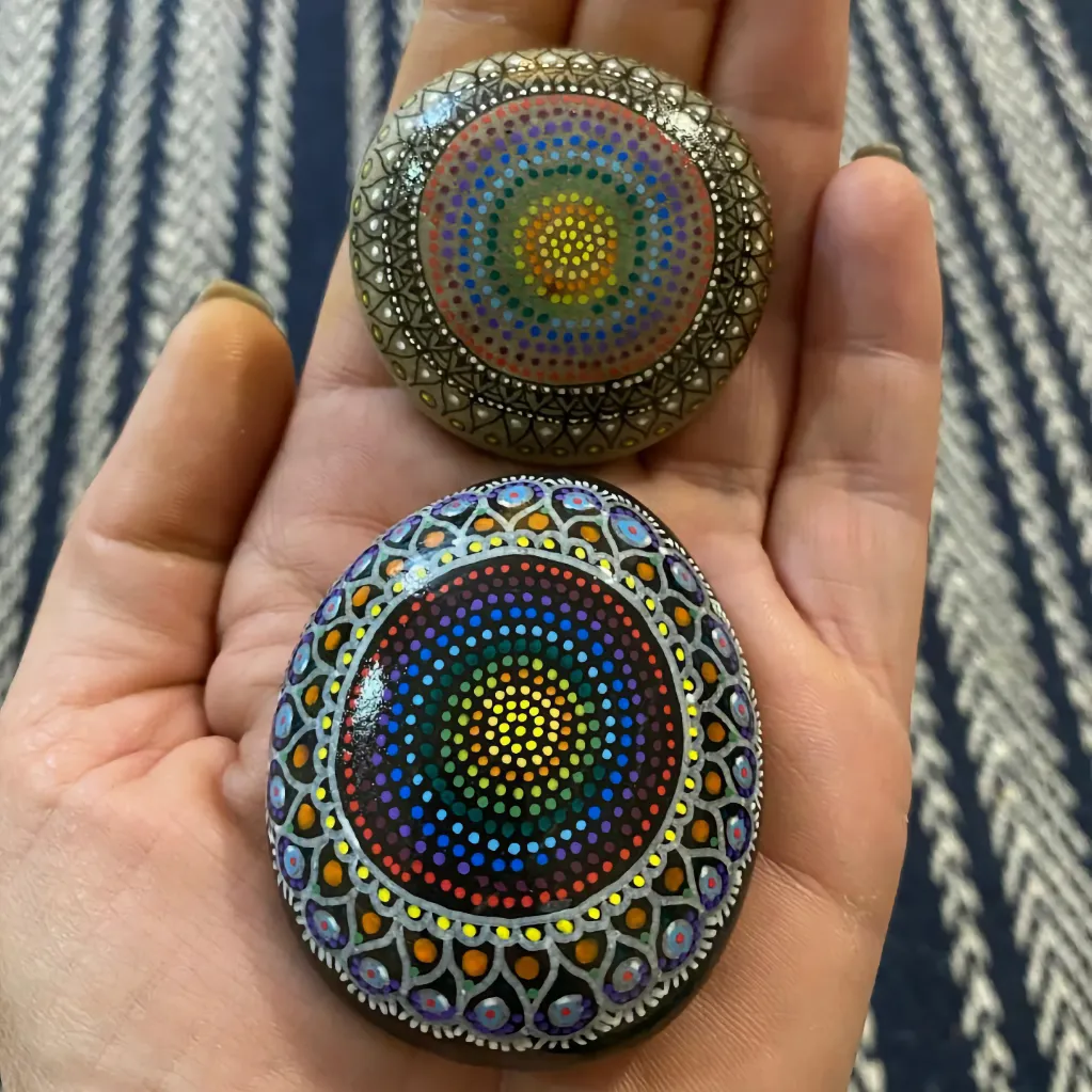 two tribal dot painted pebbles held on the fingers and palm of lady's hand