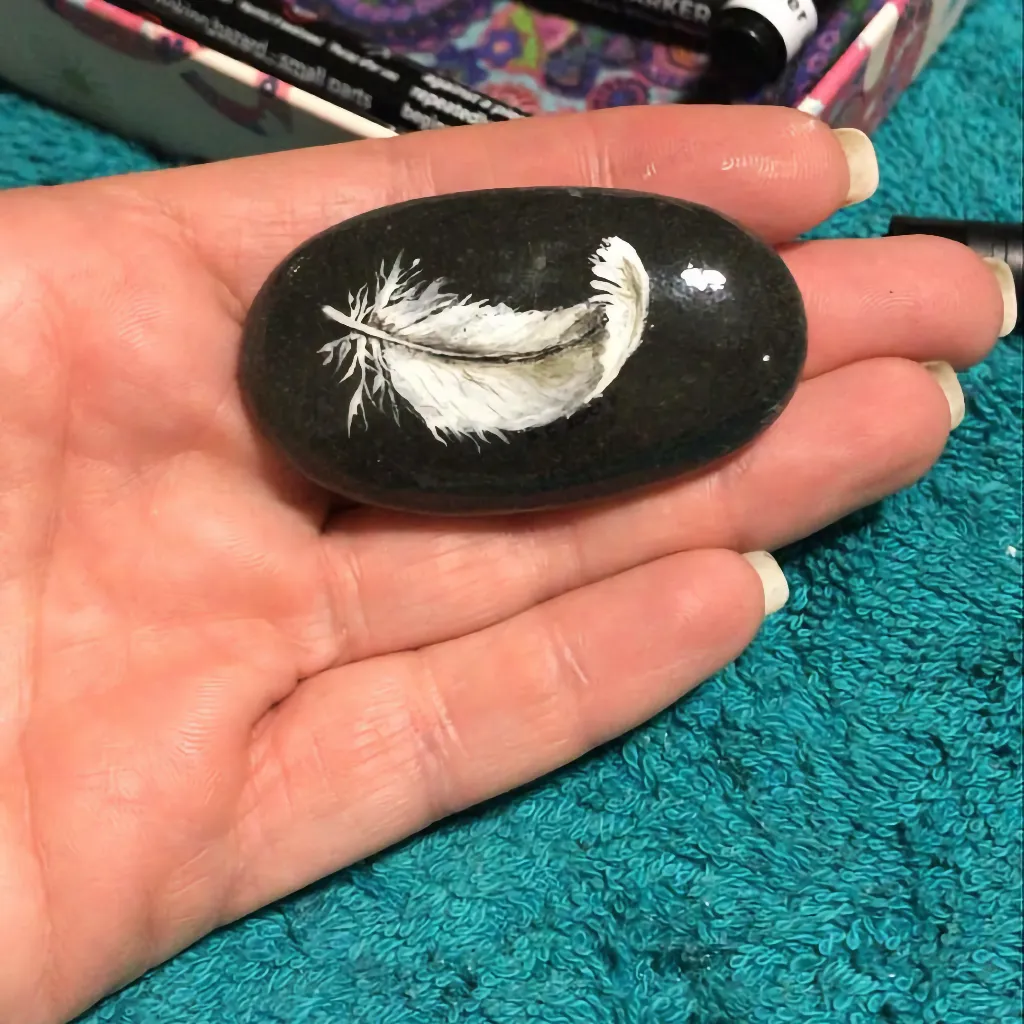 peaceful feather on almost black rock resting on the fingers of a hand