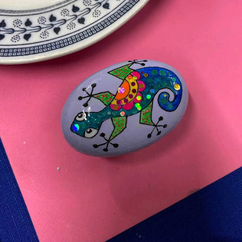 colourful gecko painted on lavender pebble on pink paper background next