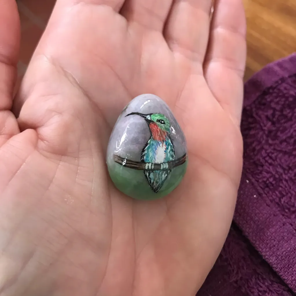 Sugarbird painted pebble in the palm of a hand