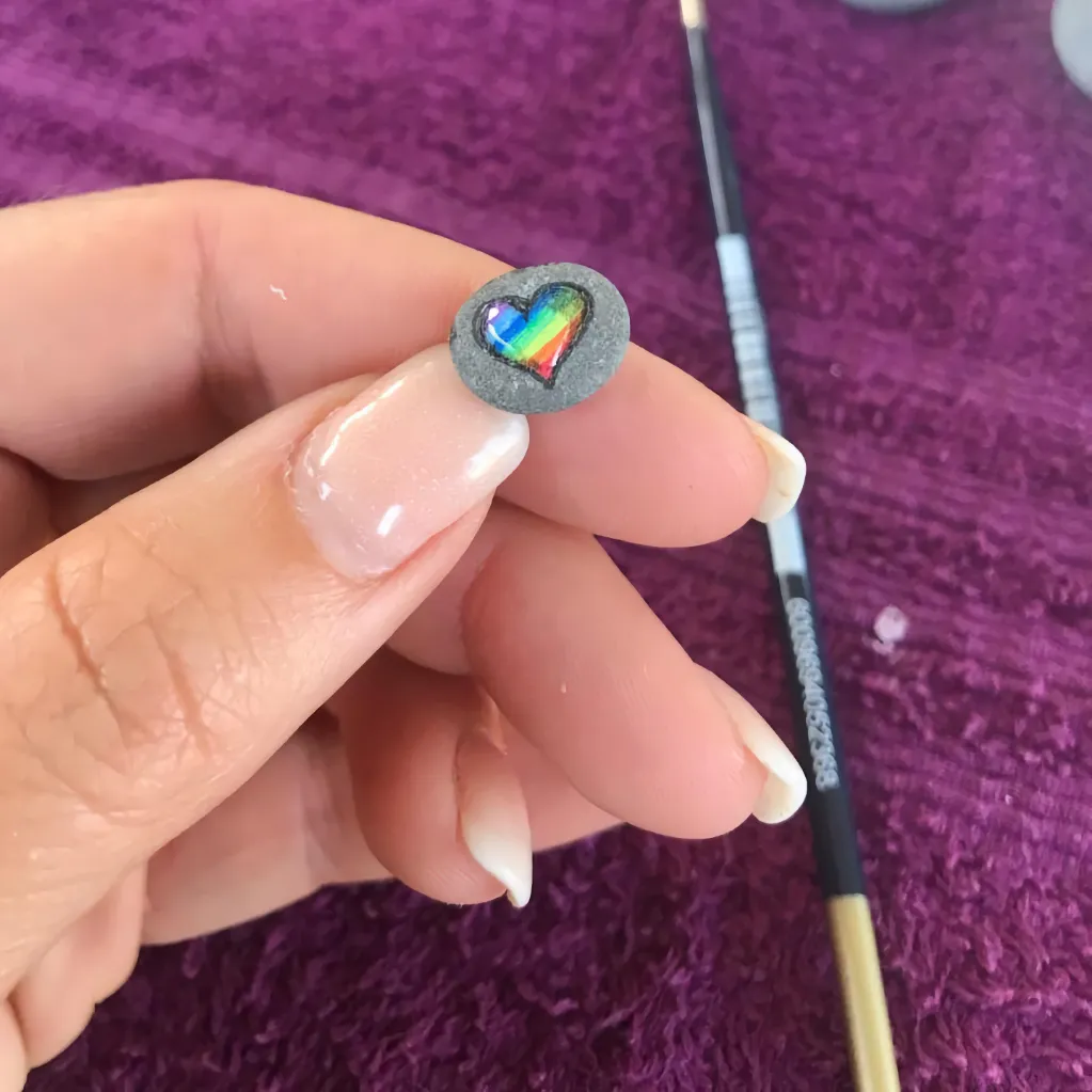 very small heart painted pebble balanced on the fingernail of the artist